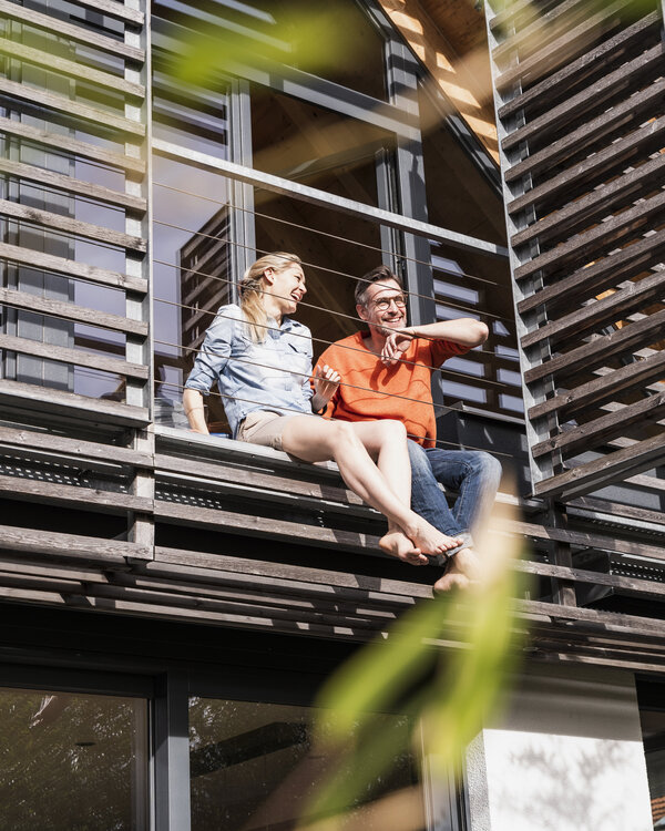 Foto eines älteren Paares auf dem Balkon seines Holzhauses.